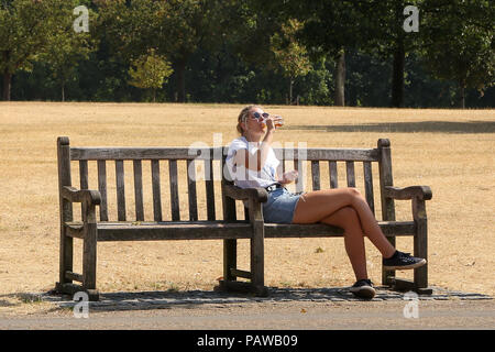 Hyde Park. Londra. Regno Unito 25 luglio 2018 - Una donna acqua potabile mentre è seduto su una panchina di Hyde Park su un molto caldi e umidi giorni nella capitale. Secondo il Met Office la temperatura a Londra e il Sud Est rischia di raggiungere 35 gradi celsius giovedì. Credito: Dinendra Haria/Alamy Live News Foto Stock