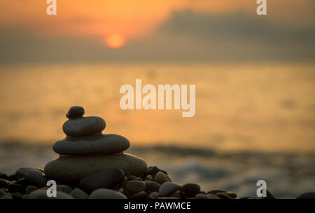 Piramide piegata Zen pietre ghiaia sul mare spiaggia al tramonto Foto Stock