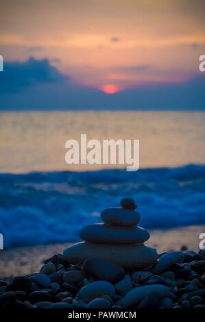 Piramide piegata Zen pietre ghiaia sul mare spiaggia al tramonto Foto Stock