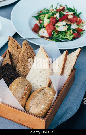 Fresco stile italiano insalata, servita in una piastra bianca e un cestello con il pane si trova accanto ad esso Foto Stock