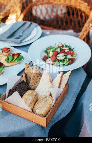 Fresco stile italiano insalata, servita in una piastra bianca e un cestello con il pane si trova accanto ad esso Foto Stock