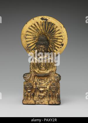 . Cultura: la Cina. Dimensioni: H. 6 1/2 in. (16,5 cm); W. 2 3/4 in. (7 cm); D. 1 3/8 in. (3.5 cm). Data: fine 4th-inizio del V secolo. Rappresentazioni di Buddha che indossa una spessa scialle su entrambe le spalle e seduta in cima a un trono con i lions su entrambi i lati sono adattamenti cinese di immagini derivate dalla regione nordoccidentale del subcontinente indiano, in particolare dalle aree nel presente-giorno del Pakistan (noto come Gandhara nel mondo antico). Esame scientifico di questa scultura ha mostrato che essa è stata colata utilizzando diversi stampi ceramici, una tecnica che è stata utilizzata anche per creare il bronzo antico Foto Stock