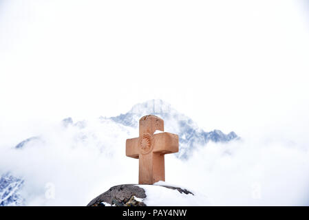 Croce Santa di pietra e Monte Kazbek innevato sullo sfondo, vicino alla Chiesa della Trinità di Gergeti, Georgia Foto Stock