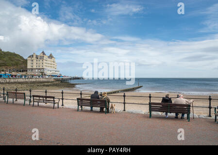 I turisti seduti sui banchi guardando al mare a Llandudno sulla costa del Galles del Nord, Regno Unito. Foto Stock