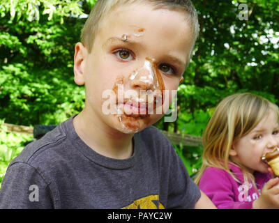 Un giovane ragazzo (6 anni) con il volto ricoperto di cioccolato dopo mangiare un gelato Foto Stock