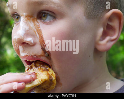 Un giovane ragazzo (6 anni) con il volto ricoperto di cioccolato dopo mangiare un gelato Foto Stock