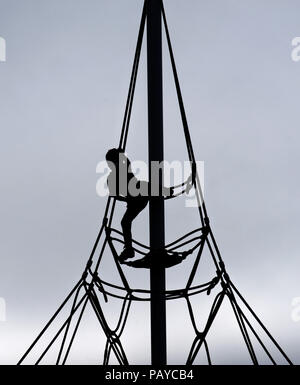 Una silhouette di un giovane ragazzo (6 yr old) su una corda di telaio di arrampicata Foto Stock