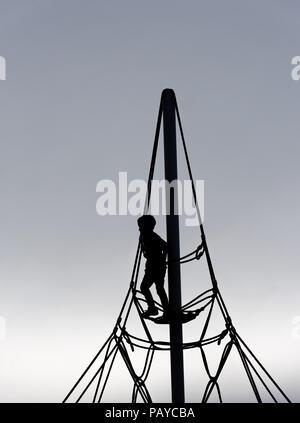 Una silhouette di un giovane ragazzo (6 yr old) su una corda di telaio di arrampicata Foto Stock