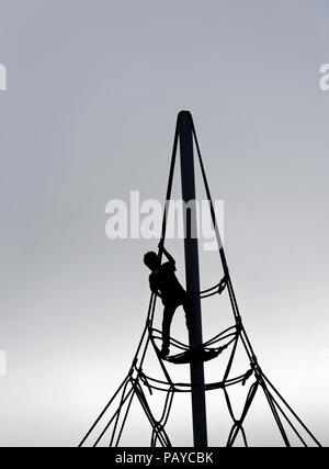 Una silhouette di un giovane ragazzo (6 yr old) su una corda di telaio di arrampicata Foto Stock