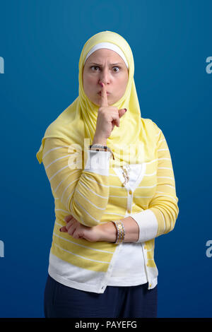 Bella donna musulmana con il silenzio gesto su sfondo blu Foto Stock