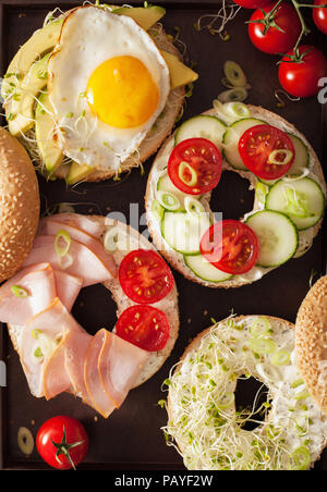 Varietà di panini su bagel: uovo, avocado, prosciutto, pomodoro, formaggio a pasta morbida, di germogli alfalfa Foto Stock