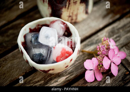 Ceramiche fatte a mano. Cubetti di ghiaccio, frutti di bosco surgelati, su sfondo in legno.la freschezza, rustico Foto Stock