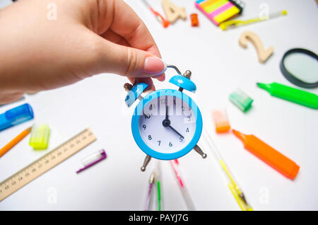 Si torna a scuola. blu sveglia sul banco di scuola nelle mani di uno studente. cancelleria. accessori. Sfondo bianco. adesivi, penne colorate, penc Foto Stock