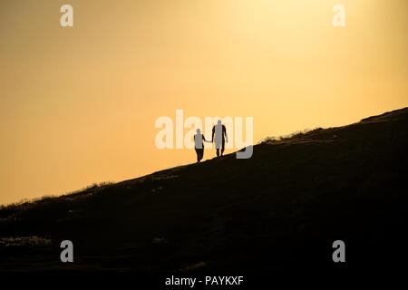 Un giovane tenendo le mani a piedi verso la sommità di una collina a guardare il tramonto Foto Stock