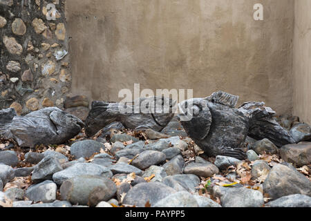 Scolpito in legno stagionato e decorazioni di pesce giacente su pietre in un'alcova contro una parete marrone all'aperto Foto Stock