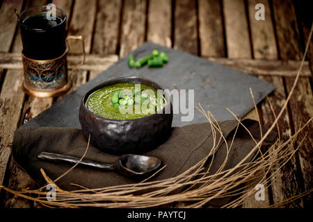 Verde zuppa di broccoli, su un piedistallo di grigio e un background in legno. Stile rustico. Semplice, nutriente cibo vegetariano. Decorate con semi. Con un tovagliolo di lino.con rami secchi e tè in un portabevande Foto Stock