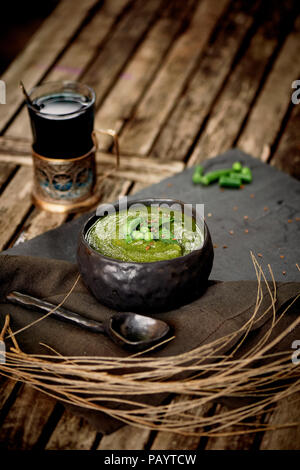 Verde zuppa di broccoli, su un piedistallo di grigio e un background in legno. Stile rustico. Semplice, nutriente cibo vegetariano. Decorate con semi. Con un tovagliolo di lino.con rami secchi e tè in un portabevande Foto Stock