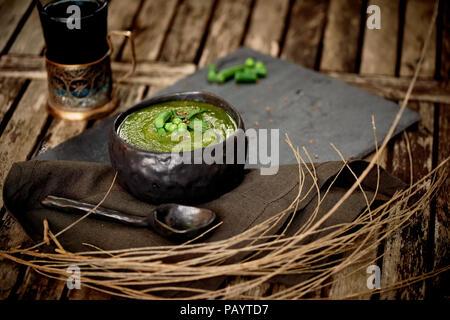 Verde zuppa di broccoli, su un piedistallo di grigio e un background in legno. Stile rustico. Semplice, nutriente cibo vegetariano. Decorate con semi. Con un tovagliolo di lino.con rami secchi e tè in un portabevande Foto Stock