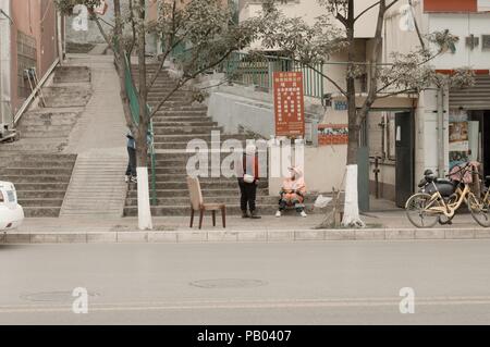 Kunming, Yunnan, Cina - 30 dicembre 2017: due donne cinesi sul marciapiede con una sedia Foto Stock