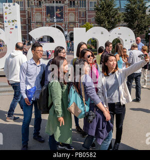 I turisti prendendo un selfie davanti alla iAmsterdam segno a piazza dei musei di Amsterdam. Foto Stock