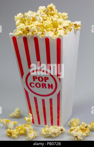 Un rosso spogliato di popcorn piccolo cucchiaio colmo di popcorn su un contatore di bianco Foto Stock