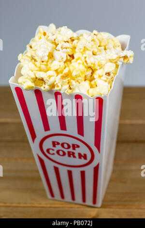 Un rosso spogliato di popcorn piccolo cucchiaio colmo di popcorn su un contatore di bianco Foto Stock
