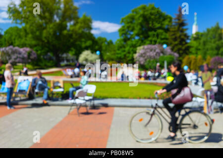 I turisti in vesti luminose a piedi nel centro di Riga tra i fiori lungo la strada cafe nel parco. Sfocata Foto Stock