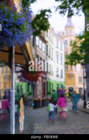 I turisti in vesti luminose a camminare per le strade di riga tra i fiori lungo le caffetterie lungo la strada e le facciate storiche. Sfocata Foto Stock