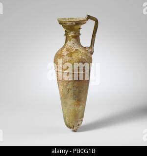 Caraffa di vetro. Cultura: Romano. Dimensioni: complessivo: 7 7/16a. (18.9cm). Data: 4th-5secolo D.C.. Traslucido giallo verde; la maniglia e sentieri nello stesso colore ma una scia di colore incerto, possibilmente bianco opaco. Cerchione piegato sopra e in; ovale, bocca svasata, con attrezzature trattini; collo ovale, si espande verso il basso; spalla spiovente; alto e snello corpo con lato rettilineo con la conicità rivolta verso il basso; fondo arrotondato con prominenti pontil tampone; impugnatura asta fissata come un tampone di grandi dimensioni a spalla, redatto e leggermente fuori e poi trasformato in e fatta cadere sulla parte superiore del cerchio. Un sentiero avvolto in senso orizzontale una volta e mezza un Foto Stock