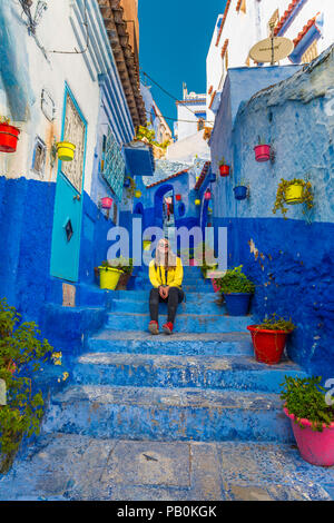 Giovane donna nella città vecchia si siede su una scala, blue house pareti, medina di Chefchaouen, Chaouen, Tangier-Tétouan Foto Stock