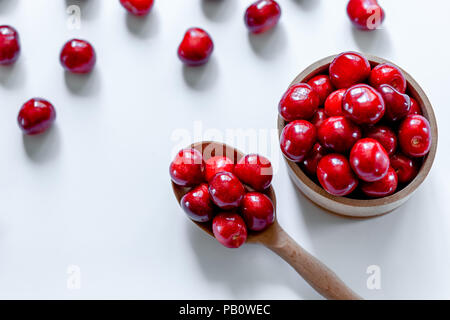 Red ciliegie mature con il cucchiaio di legno su sfondo bianco. Lay piatto. Concetto di cibo. Foto Stock