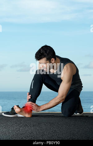 Atleta con dolore alla caviglia in background con mare spazio per il testo Foto Stock