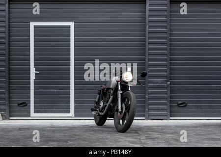 Custom Moto parcheggio vicino al nero edificio industriale. Tutto è pronto per il divertimento alla guida della strada vuota su un motociclo in viaggio. Hipst Foto Stock