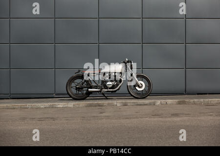 Fatte a mano in moto parcheggio vicino al muro grigio delle finanze edificio. Tutto è pronto per il divertimento alla guida della strada vuota su un motociclo in viaggio. Foto Stock