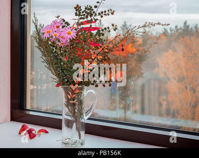 Sul davanzale della finestra in un decanter di vetro autunno magnifico bouquet di fiori e di Bright Foglie di autunno. Foto Stock