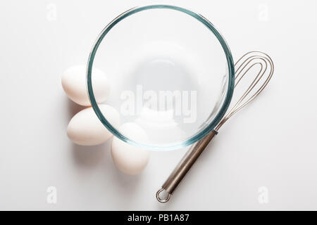 Trasparente come il vetro ciotola con baffo di metallo e tre le uova bianche a parte direttamente dal di sopra Foto Stock