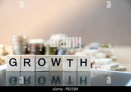 La crescita parola scritta nel cubo di legno la riflessione su Black mirror con monete stack come grafico in background Foto Stock