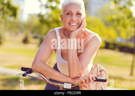 Bella donna senior per trasmissione via IR mentre appoggiata sulla bicicletta Foto Stock