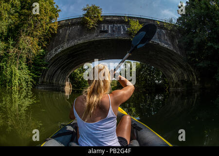 Una donna bionda pagaie un kayak gonfiabili lungo il fiume Avon nel Somerset durante l'estate. Foto Stock