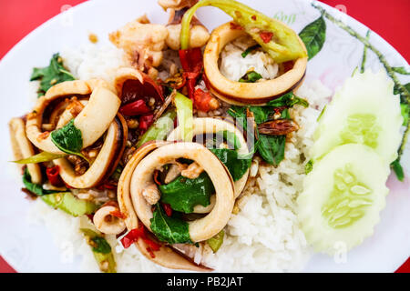 Il riso condito con stir-pesce fritto e basilico sul piatto bianco sfondo rosso Foto Stock