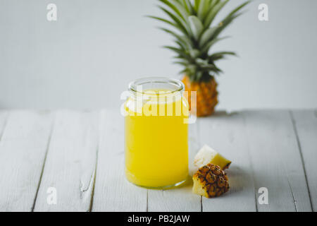 Succo di ananas in una bottiglia di vetro bianco sullo sfondo di legno Foto Stock