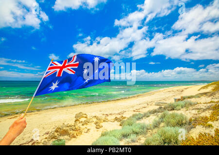 Bandiera australiana sventolando in primo piano con il paesaggio costiero della piscina Mettams, Trigg Beach, spiaggia Nord vicino a Perth in Australia Occidentale. Turismo in Australia. Foto Stock