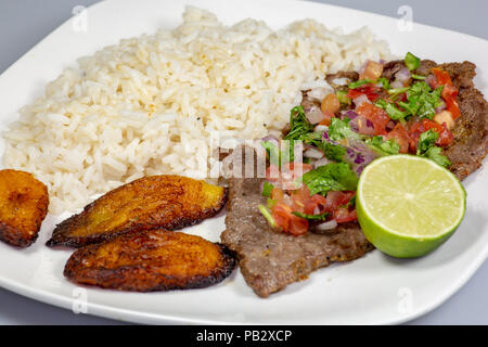 Una bistecca coperto di Pico de Gallo circondato da platani e riso bianco su una piastra bianca. Cibo cubano. Foto Stock