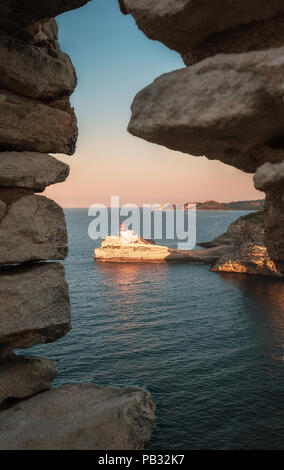 La mattina presto la luce solare sulla "Phare de la Madonetta' faro all'ingresso al porto di Bonifacio in Corsica vista attraverso una finestra di un vecchio sto Foto Stock