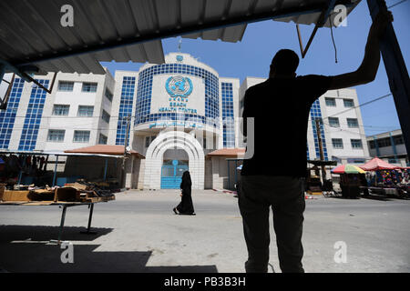 La striscia di Gaza City, nella Striscia di Gaza. 26 Luglio, 2018. Palestinesi a piedi passato la spiaggia Centro Salute edificio dell'Ente soccorso e lavori delle Nazioni Unite per i profughi della Palestina nel Vicino Oriente (UNRWA) come il personale dell'Agenzia hanno iniziato il loro sciopero generale in una reazione al recente lavoro eliminazioni e il downgrade dei contratti, nella città di Gaza, Striscia di Gaza, 26 luglio 2018. Credito: Wissam Nassar/dpa/Alamy Live News Foto Stock