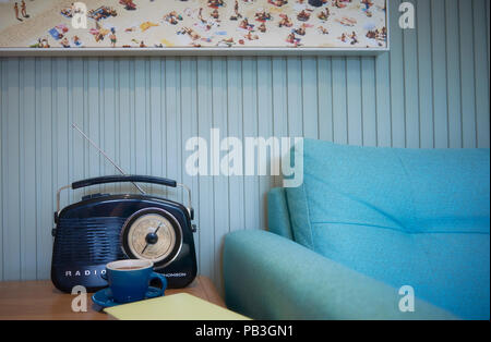 Una radio e una tazza di tè accanto a un lettino di teal Foto Stock