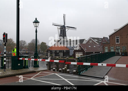 Una barriera e la luce rossa significa la apertura di un ponte sul fiume Spaarne in Haarlem, Paesi Bassi. Il De Adriaan mulino a vento (Molen de Adriaan) Foto Stock