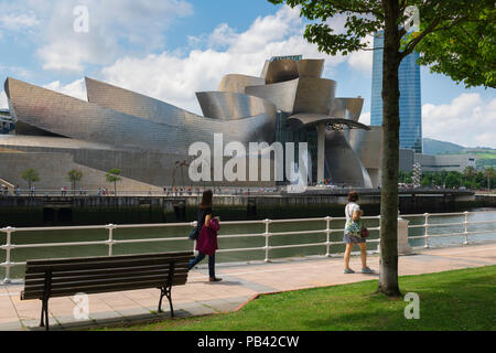 Bilbao Spagna Città, due giovani donne di guardare attraverso il Museo Guggenheim edificio come essi potrete passeggiare lungo il fiume nel centro di Bilbao, Spagna. Foto Stock