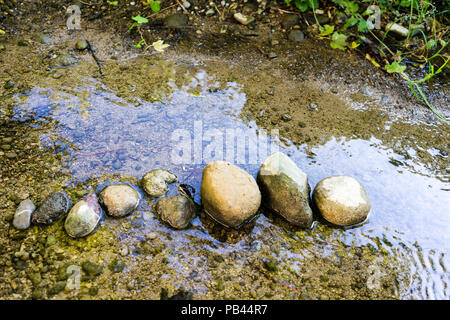 Pietre schierate nella piccola insenatura con acqua la riflessione Foto Stock