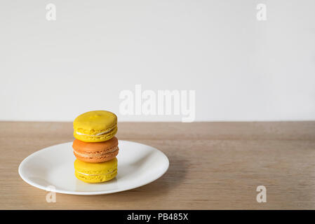 Ripresa in grandangolo di arancione e giallo Macaron torre su una piastra bianca, contatore di legno e sfondo luminoso Foto Stock